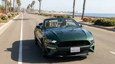 Person driving a white car rental along a scenic coastal highway in California