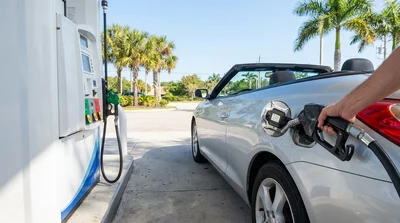 White car rental parked next to a gas station fuel pump under palm trees in Florida