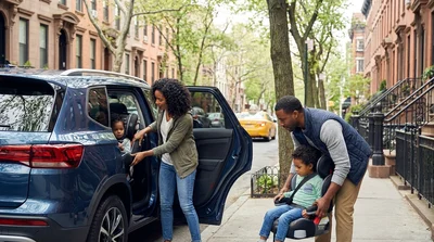 Child in a booster seat inside a car rental parked on a busy New York street