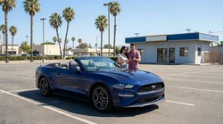 A traveler checking their watch next to a vehicle at a car rental lot in California