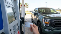 Person inserting a credit card into a gas pump terminal next to a car rental in Texas
