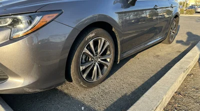 Close-up of a damaged alloy wheel on a car rental parked next to a concrete street curb in California