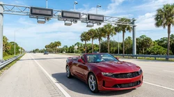 White car rental driving through an electronic toll plaza on a sunny Florida highway