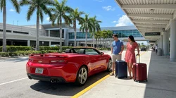 Red convertible car rental parked next to tall palm trees on a sunny beach in Florida
