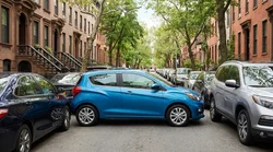 Small car rental parallel parked on a busy New York street with tall buildings in the background