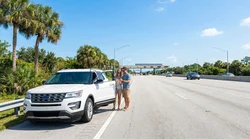 Smartphone showing a GPS map on the dashboard of a car rental driving toward a Florida highway toll booth