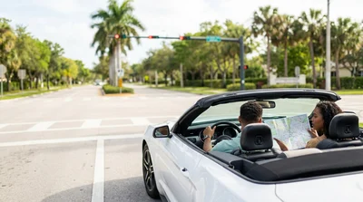 Person driving a car rental on a sunny highway lined with palm trees in Florida