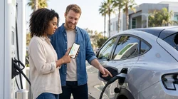 Driver using a mobile phone app beside a plugged-in electric car rental at a California charging station