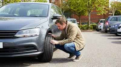 Person inspecting the windscreen and front tyre of a car rental parked on a sunny street in Pennsylvania