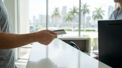 Customer handing a credit card to a car rental agent at a checkout desk in Miami