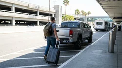 Traveler walking with luggage towards a white SUV in a Texas airport car rental lot