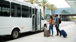 Passengers loading luggage onto a shuttle bus at an Orlando airport car hire facility