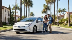 White hybrid car rental driving on a sunny Los Angeles road lined with palm trees