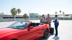 Traveler loading luggage into a vehicle at a car rental lot in Los Angeles