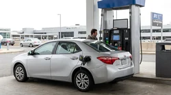 A person pumping fuel into a white car hire at a gas station in New York