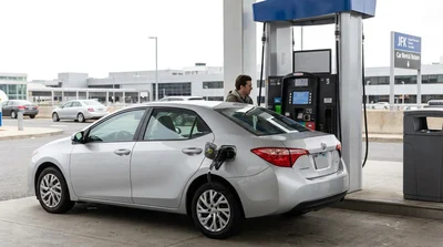 A person pumping fuel into a white car hire at a gas station in New York