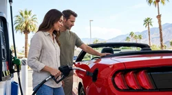 Driver holding a fuel nozzle to fill up a white car hire at a gas station in California