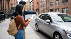 Person using a smartphone inside a parked car rental on a New York street