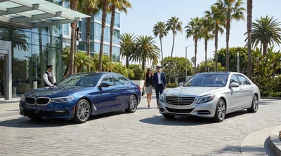 Sleek black luxury car hire parked on a sunny palm tree-lined street in Los Angeles