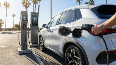 Person plugging a charging connector into a white electric car rental at a sunny California station
