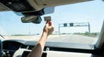Silver car rental driving under an electronic highway toll gantry on a sunny day in Texas