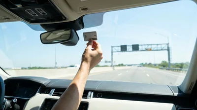 Silver car rental driving under an electronic highway toll gantry on a sunny day in Texas