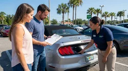 Person checking a clipboard next to a parked vehicle at a car rental lot in Orlando