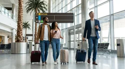 Travelers with rolling luggage walking through a busy terminal toward the car hire center at Miami Airport