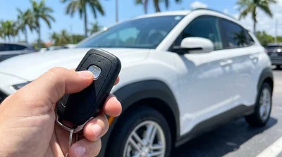 Close-up of a hand holding a key fob inside a car rental parked near a sunny Florida beach