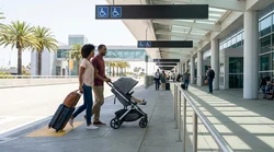 Passenger with luggage on a step-free walkway outside a Los Angeles airport terminal heading to a car hire shuttle