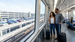 Passengers with suitcases exiting a JFK AirTrain in New York under a sign pointing to the car rental center