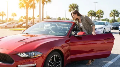 Person checking the windshield of a car rental for a toll transponder in a sunny Florida parking lot