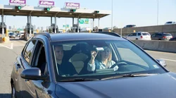 Silver car rental driving under an electronic toll gantry on a New York highway