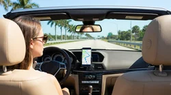 Smartphone displaying a navigation map mounted on the dashboard of a car rental driving past palm trees in Florida