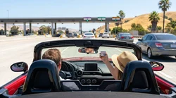 Silver car rental passing under an electronic toll reader on a sunny California highway
