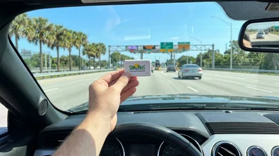 SunPass transponder attached to the windshield of a car rental on a sunny Florida highway
