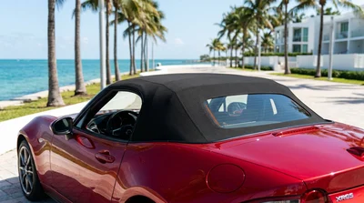 Red soft top convertible car rental parked near a beach lined with palm trees in Miami