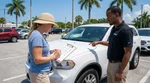 Person reviewing a car rental damage diagram on a clipboard beside a parked vehicle in sunny Florida
