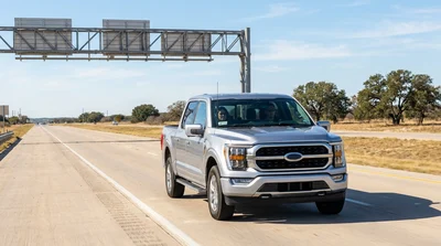 A white car rental driving under an electronic toll sign on a Texas highway