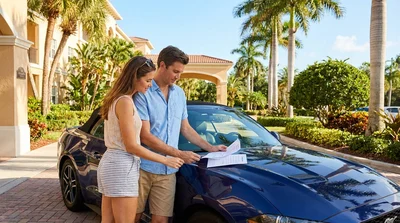 A white car rental driving along a sunny coastal road lined with palm trees in Florida