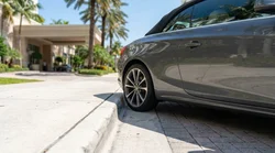 Low angle view of a white car rental parked tightly against a concrete kerb in Miami