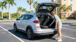 Person checking the open trunk of a car rental parked along a sunny coastal road in Florida