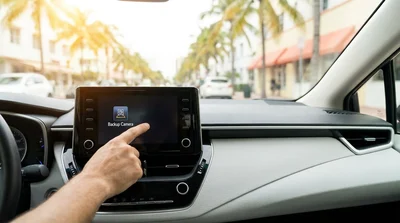 Close up of a dashboard reversing camera screen inside a Miami car rental parked near palm trees