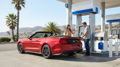 Person pumping fuel into a white car rental at a sunny California gas station