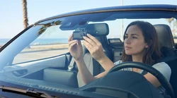 Small black dash cam mounted on a car rental windscreen facing a sunny California highway
