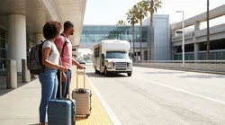 A shuttle bus parked outside a Los Angeles car rental center with passengers loading their luggage