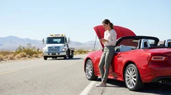 Person looking under the open hood of a broken down car rental on a desert highway near Las Vegas