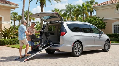 A mobility scooter next to the open trunk of a spacious car rental parked on a sunny Florida street