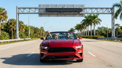 Silver car rental approaching an electronic toll booth on a sunny Florida highway
