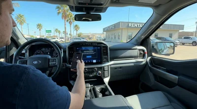 Person touching an infotainment screen while holding a smartphone inside a Texas car rental